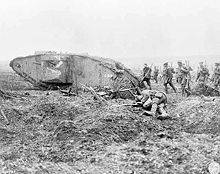 Group of armed soldiers march past a wrecked tank and a body