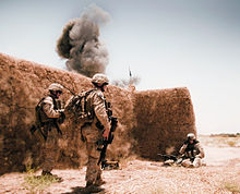 Marines beside a mud wall as an explosion goes off behind it